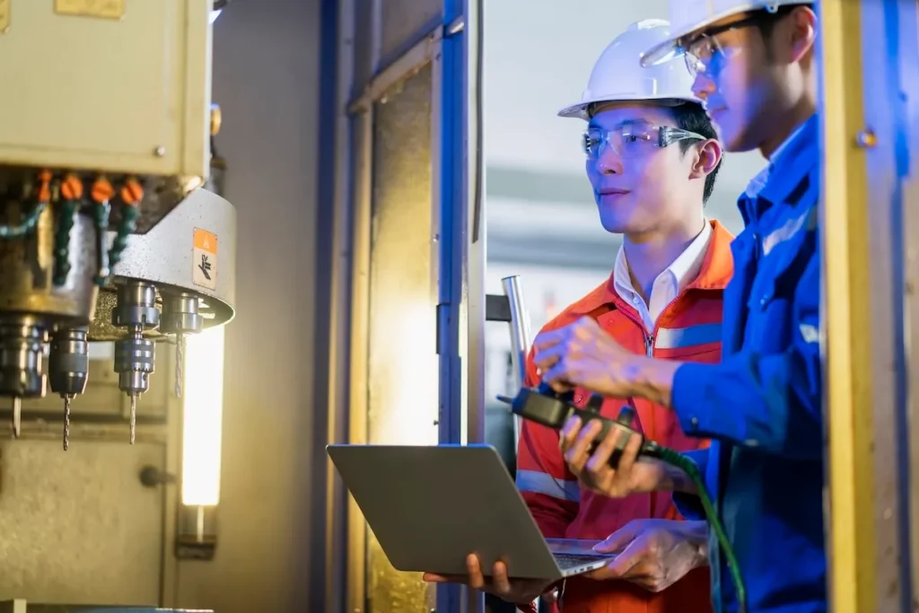 Hai kỹ sư châu Á kiểm tra máy móc và trao đổi công việc trong nhà máy
