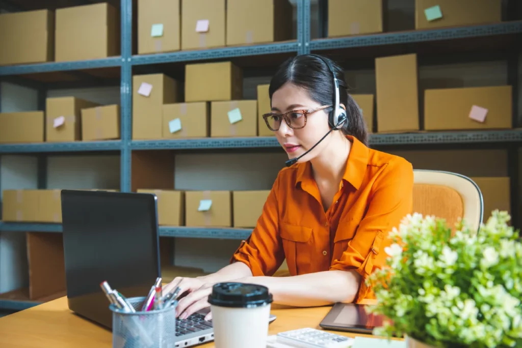 Điều phối viên Logistics đeo tai nghe xác nhận lịch vận chuyển trên máy tính
